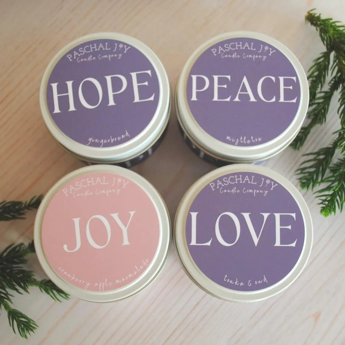 Four candles with lids labeled 'Hope', 'Peace', 'Joy', and 'Love' on a wooden surface.