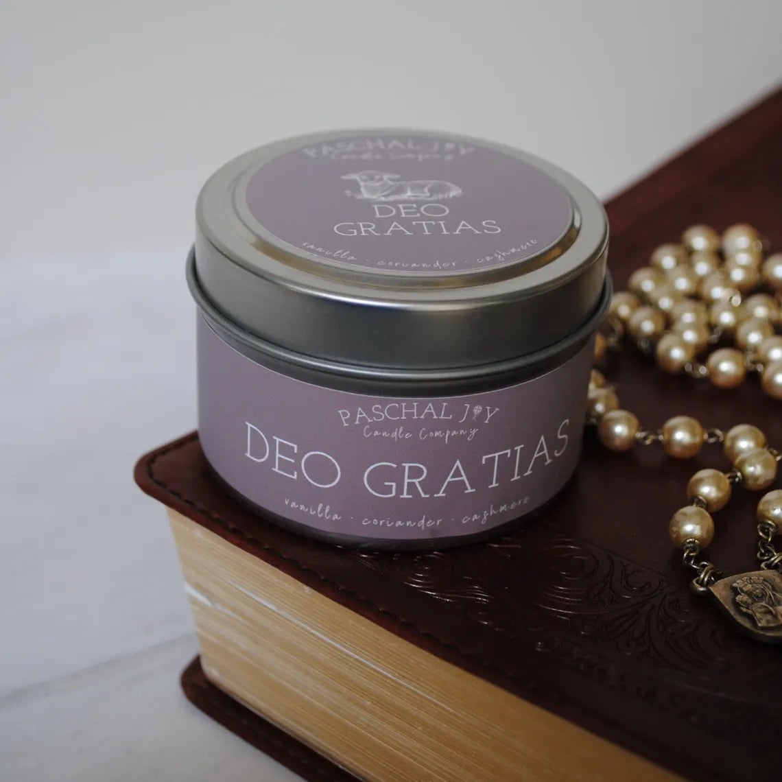 Candle container labeled 'Deo Gratias' on a book with pearls beside it