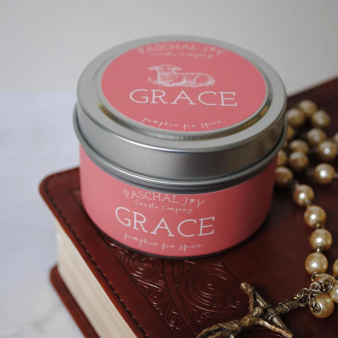 Grace scented candle tin with rosary on top of a brown bible