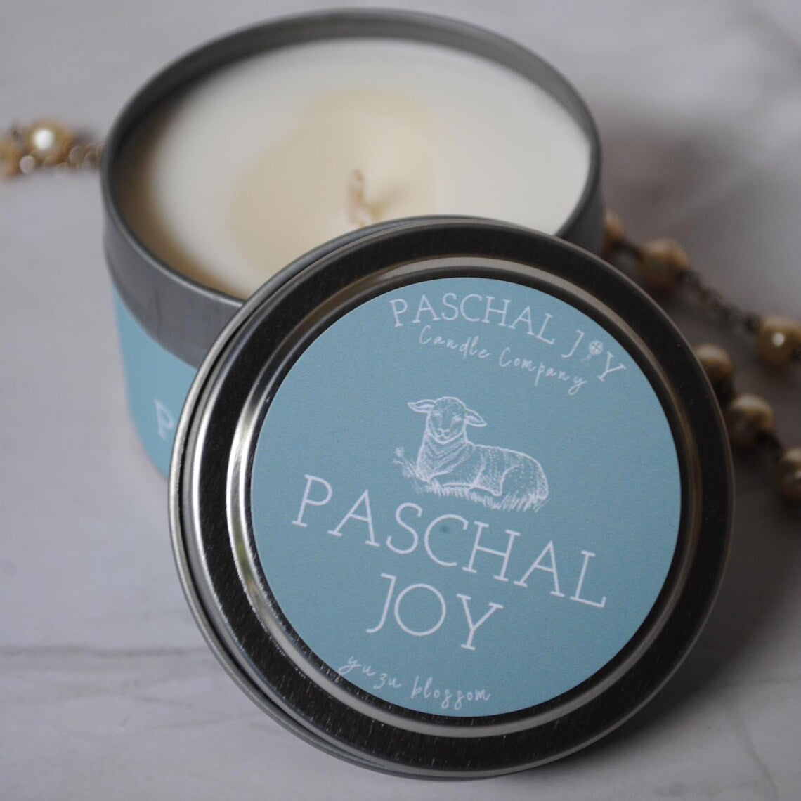 Candle in a tin with 'Paschal Joy' label on a light background
