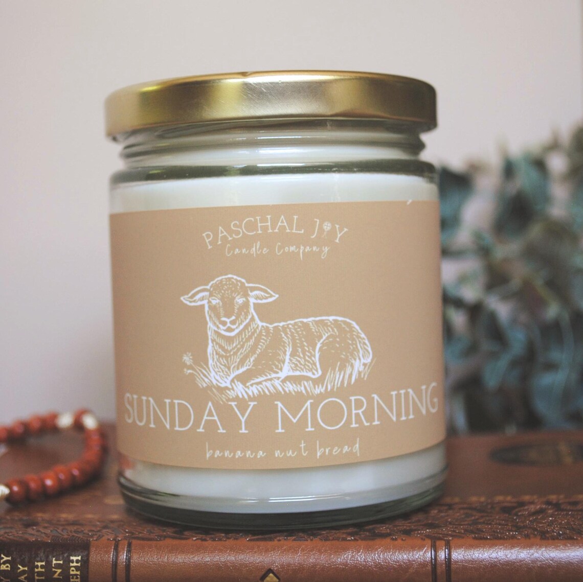 Candle jar with 'Paschal Joy Candle Company' label featuring a sheep illustration on a wooden surface.