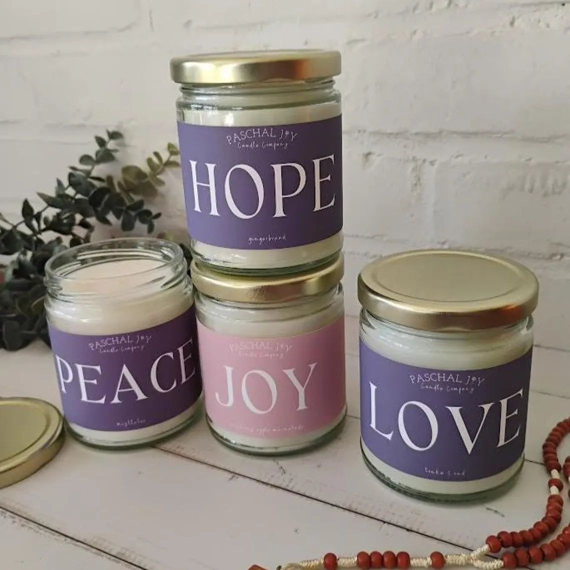 Four Advent candles with labels 'Hope', 'Peace', 'Joy', and 'Love' on a white surface.