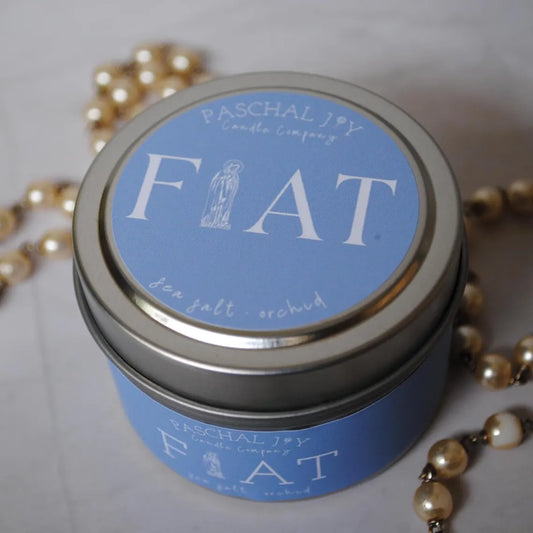 Candle tin labeled 'FIAT' with Paschal Joy Candle Company branding, surrounded by pearl rosary on a light background.