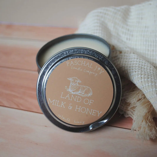 Land of Milk and Honey Candle Tin. Soft white cloth in background with a brown wood ground.