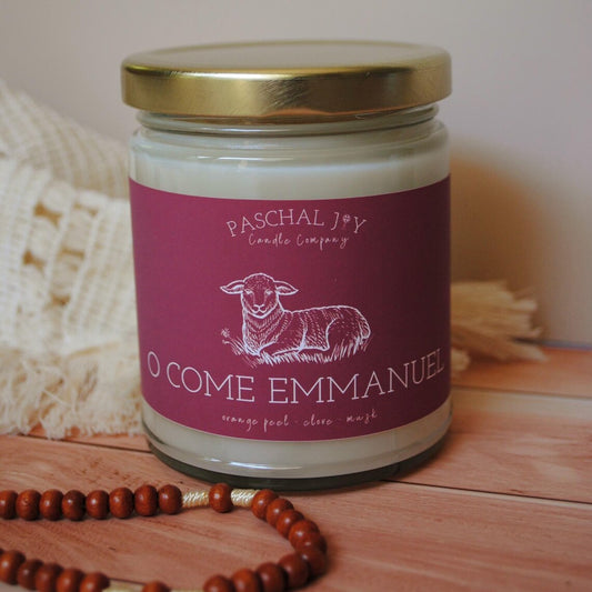 Candle jar with a red label featuring a sheep illustration and text, on a wooden surface.