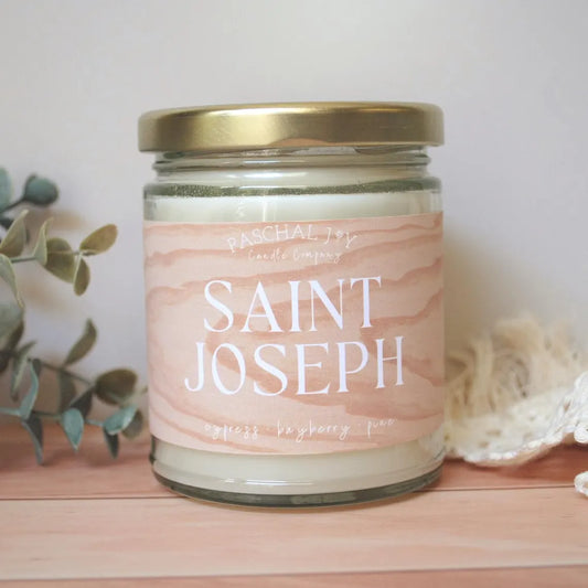 Saint Joseph scented candle on wood background with leaves and cream cloth