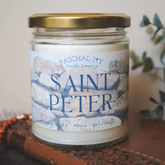Saint Peter Scented Candle on top of brown book with rosary and leaves