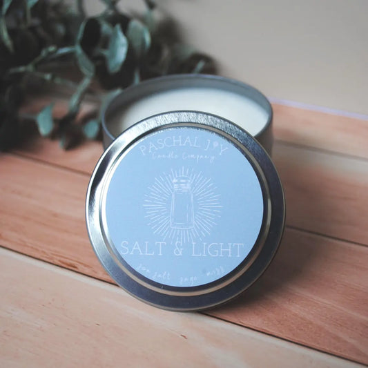 Candle in a tin with 'Salt & Light' branding on a wooden surface
