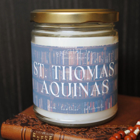 Candle jar labeled 'St. Thomas Aquinas' on a wooden surface with a dark background