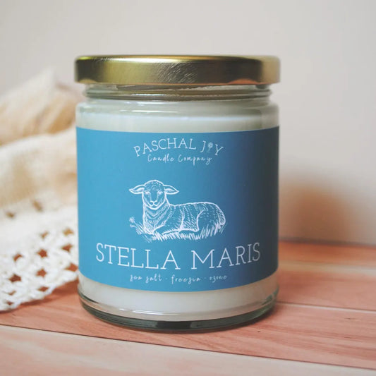 Stella Maris Blue candle jar. The candle is on a wood floor with a soft cream cloth in the background.