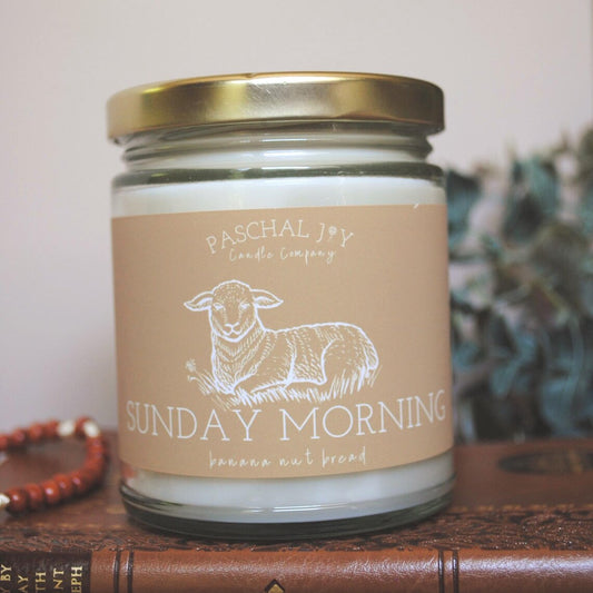 Candle jar with 'Paschal Joy Candle Company' label featuring a sheep illustration on a wooden surface.