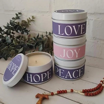 Stack of advent candles in metal tins with 'Love', 'Joy', and 'Peace' text on a wooden surface.