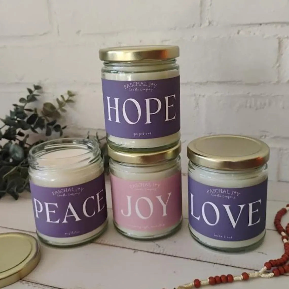 Four advent candles with labels 'Hope', 'Peace', 'Joy', and 'Love' on a white surface.