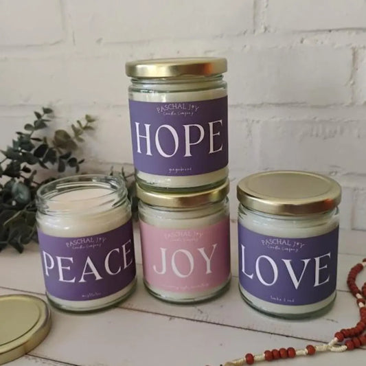 Four advent candles with labels 'Hope', 'Peace', 'Joy', and 'Love' on a white surface.