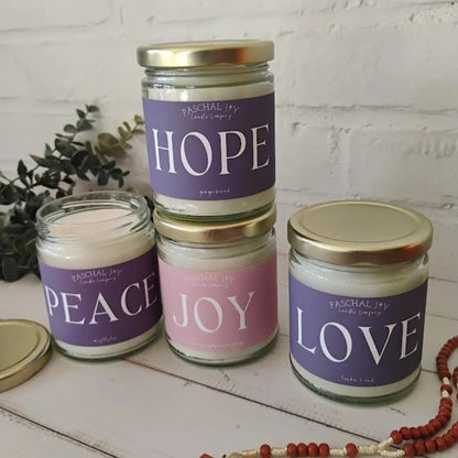 Four Advent candles with labels 'Hope', 'Peace', 'Joy', and 'Love' on a white surface.